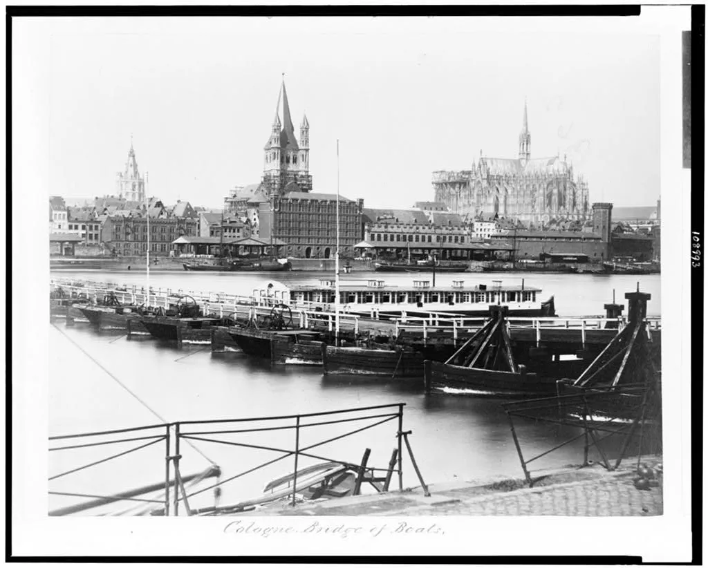 Historische Schiffbrücke mit Booten und Kölner Dom am Rheinufer.
