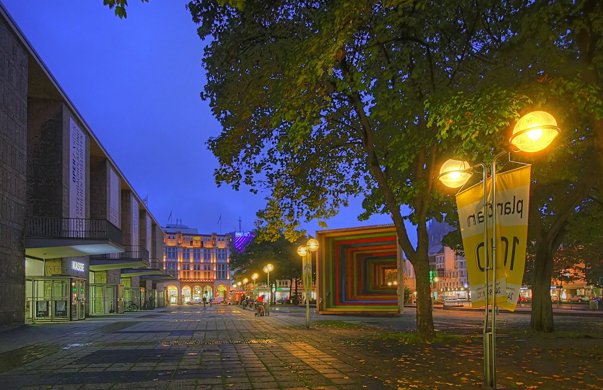 Offenbachplatz am Abend: Links die Eingangstüren in das Kölner Opernhaus, in der Mitte die SEHSTATION .