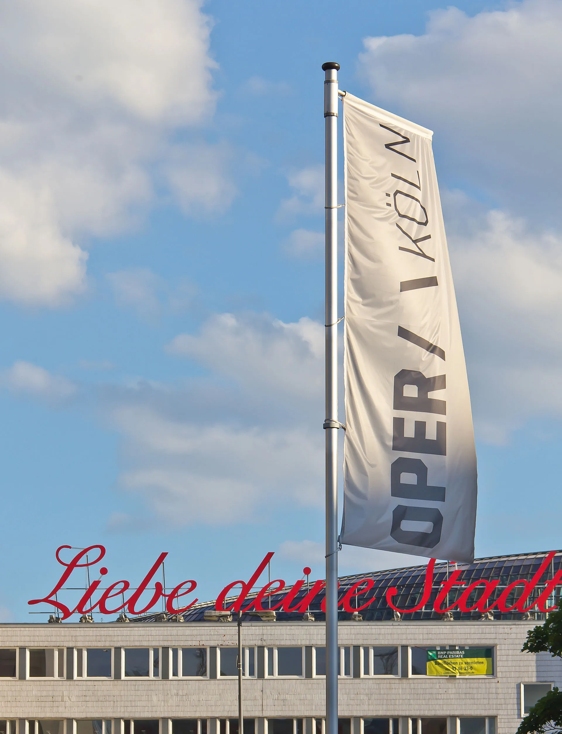 Sculpture "Love your city", in front of it a flag of the Opera Cologne